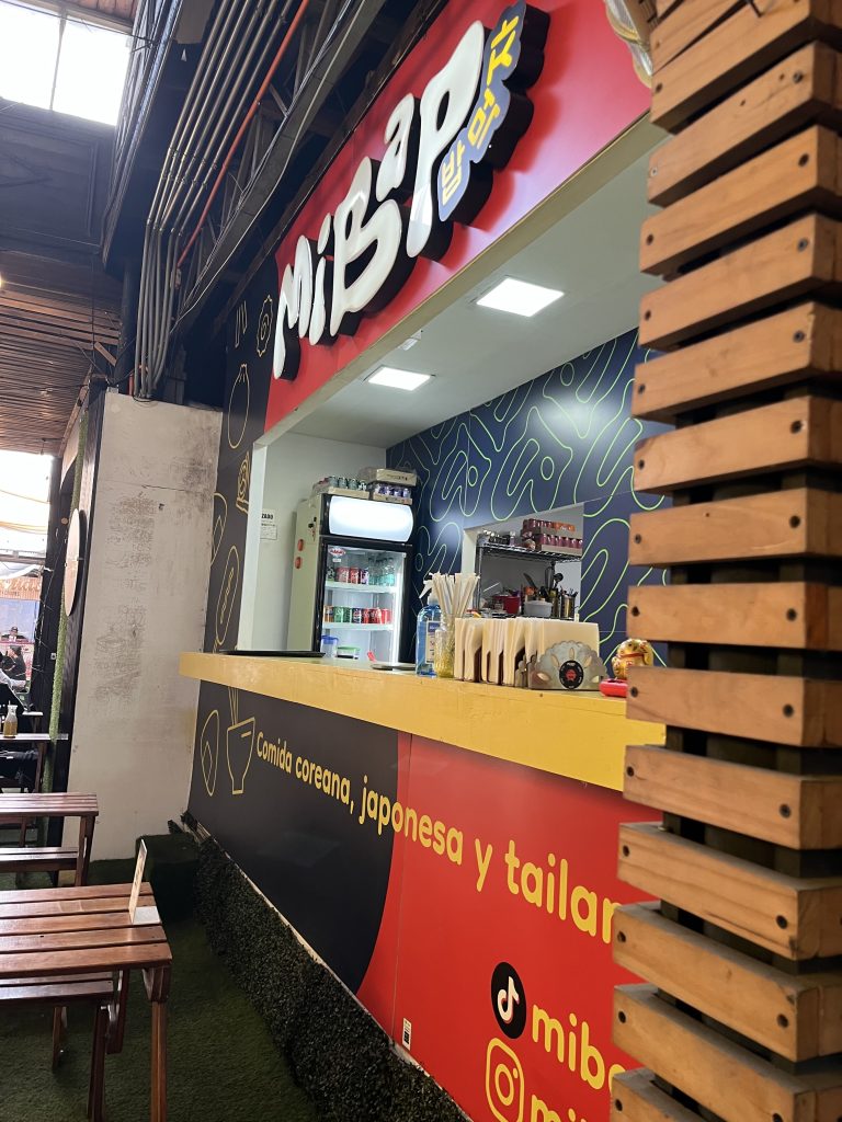 Foto del local de comida. Lugar del costado, cerca de las mesas. Se ven los jugos que ofrecen y los platos para ser repartidos.