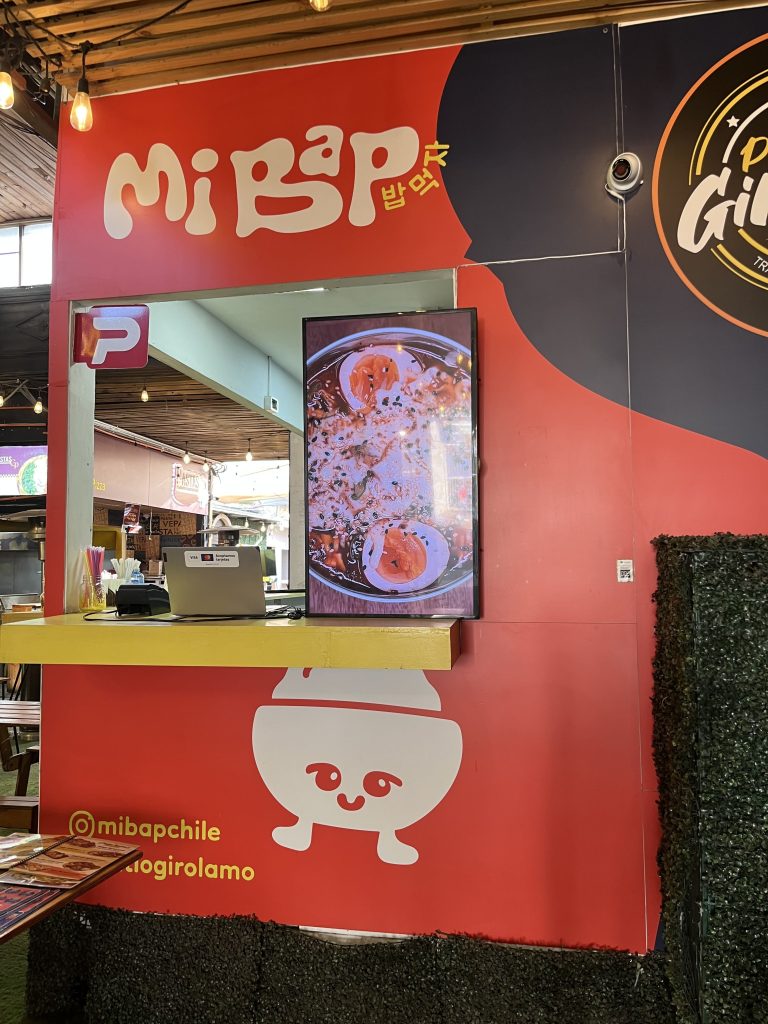 Entrada al local de comida. Además, de ser el lugar de caja. Tiene una pantalla donde se muestran algunos productos y una cámara de seguridad.