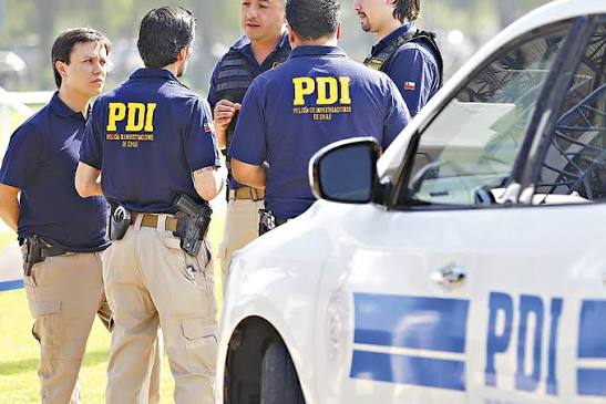 Trabajadores de la Policía de Investigaciones junto a un auto, hablando entre sí.