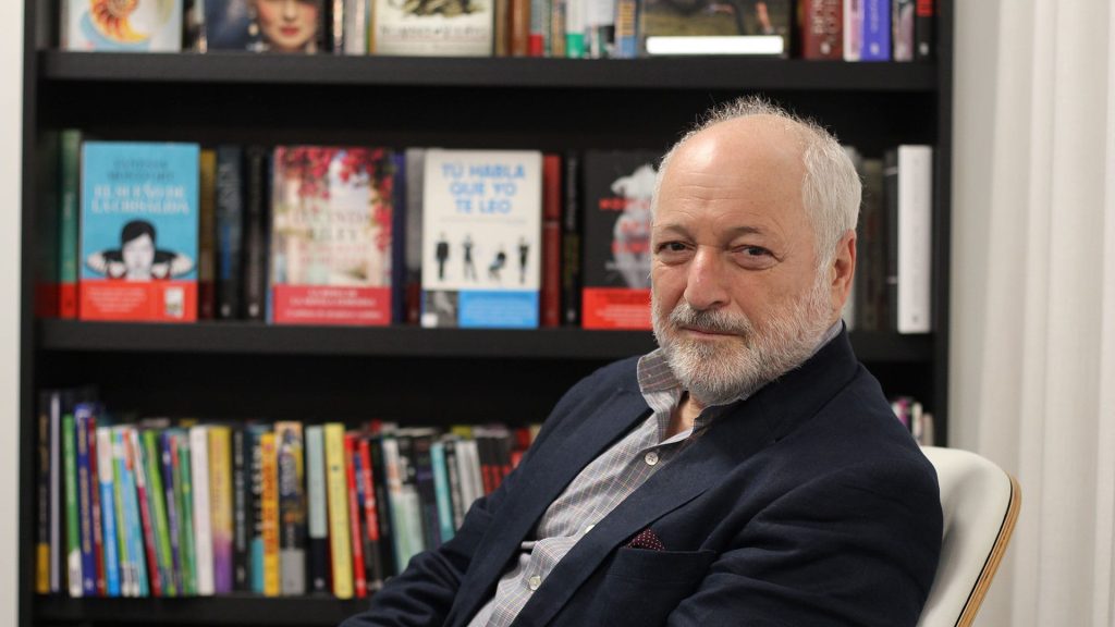 Fotografía de André Aciman con una biblioteca en el fondo.