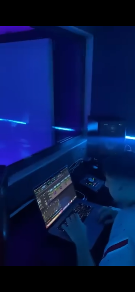 Cabina de grabación de un estudio musical con un micrófono de condensador, paneles acústicos e iluminación LED en tonos azules y violetas.