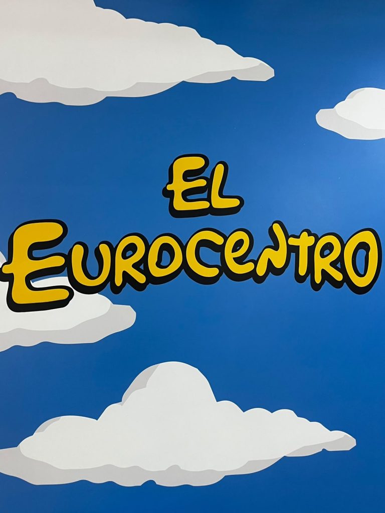 Letrero con el nombre "El Eurocentro" en una pared con fondo azul y nubes.