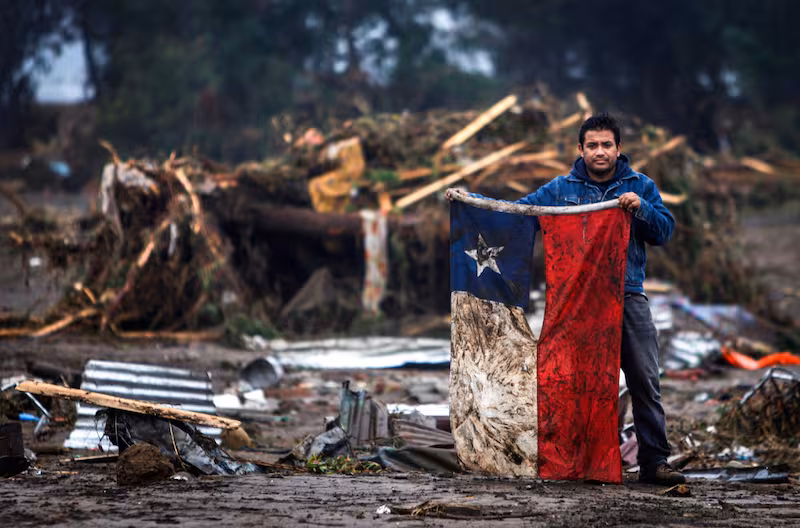 Hombre chileno enseñando la bandera de nuestro país rodeado de escombros debido al terremoto del 27 de febrero del año 2010